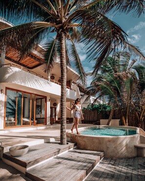 A poolside area with a palm tree, a pool, and a building with large windows and a balcony. - Zorba Tulum Beach Homes (Tulum)