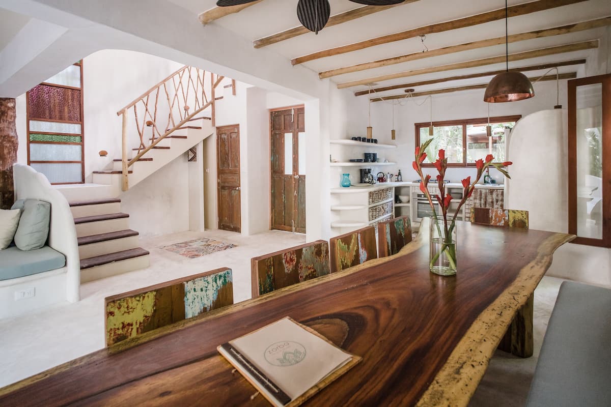A spacious living area with a wooden dining table, a staircase, and a view of the outdoors.