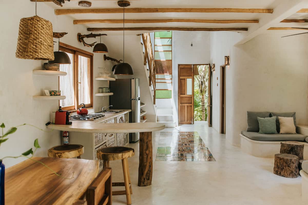 A spacious kitchen with wooden beams, a dining area with stools, and a cozy seating area with cushions.
