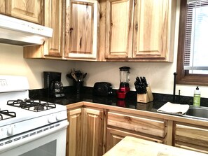 A kitchen with wooden cabinets, a gas stove, a coffee maker, a blender, and a knife block.