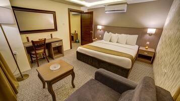Habitación de hotel con cama, escritorio, silla, sofá, mesita de noche y velador.