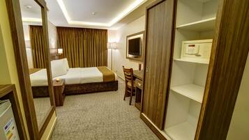 A hotel room with a bed, a desk, a chair, a TV, a microwave, and a wardrobe.
