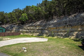 A concrete patio area with a grassy foreground and a rocky cliff in the background. - Pipe Creek Ranch | Pets ok | Hot Tub | Sleeps 3 (Pipe Creek)