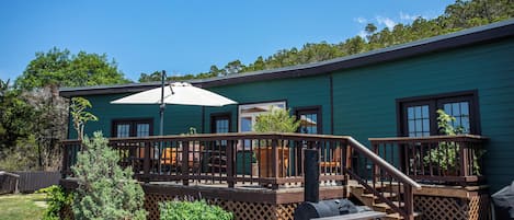 Ein grünes Gebäude mit einer Terrasse, Sitzgelegenheiten im Freien und einem Grillbereich.