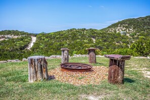 A rustic outdoor setting with a metal fire pit surrounded by wooden posts and a gravel area. - Pipe Creek Ranch | Pets ok | Hot Tub | Sleeps 3 (Pipe Creek)
