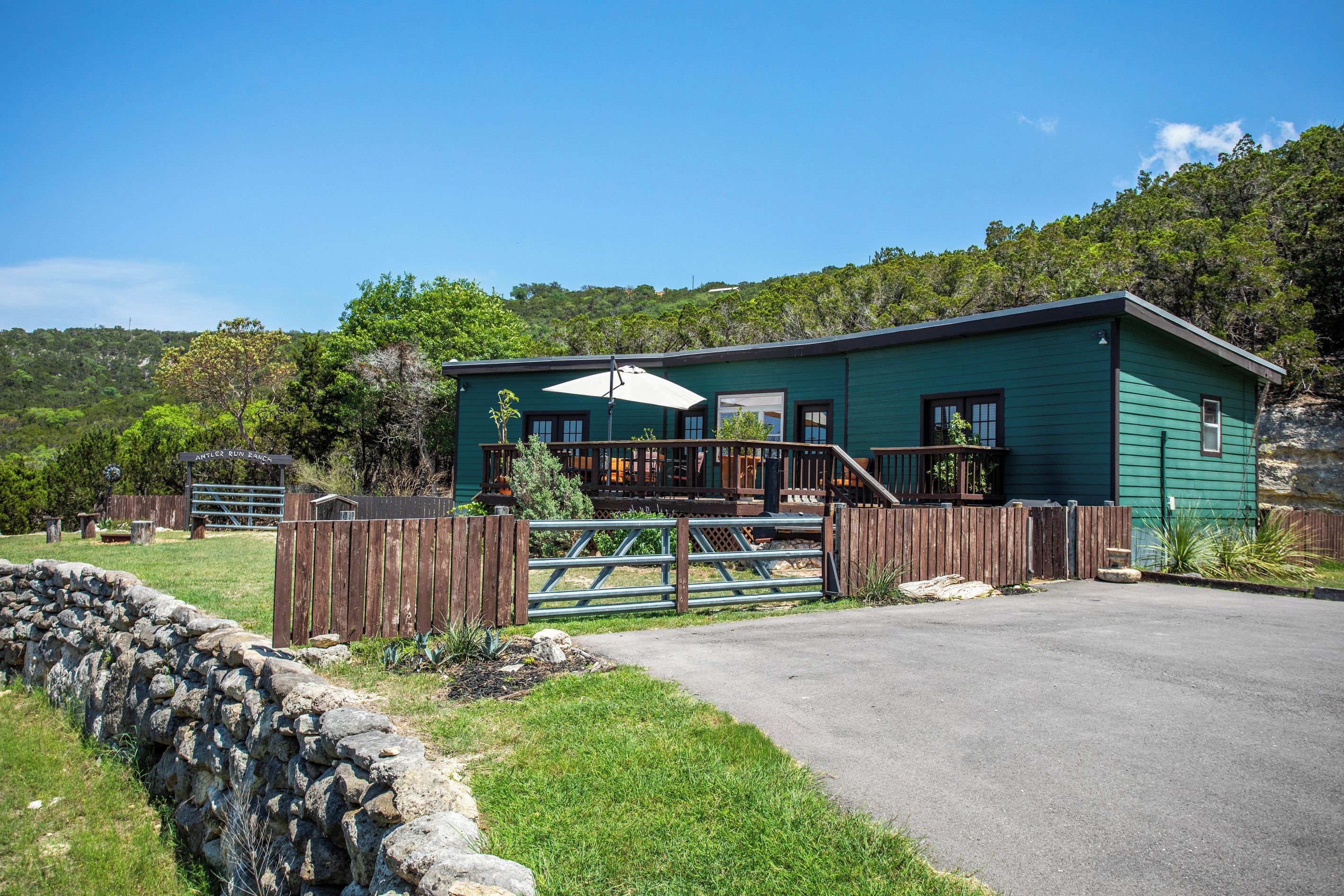 A green building with a porch, a stone wall, and a fenced area.