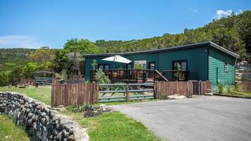 A green building with a porch, a stone wall, and a fenced area.