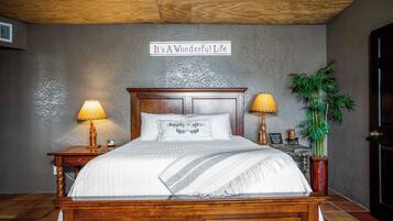 A bedroom with a wooden bed, two bedside lamps, a sign above the bed, and a potted plant.