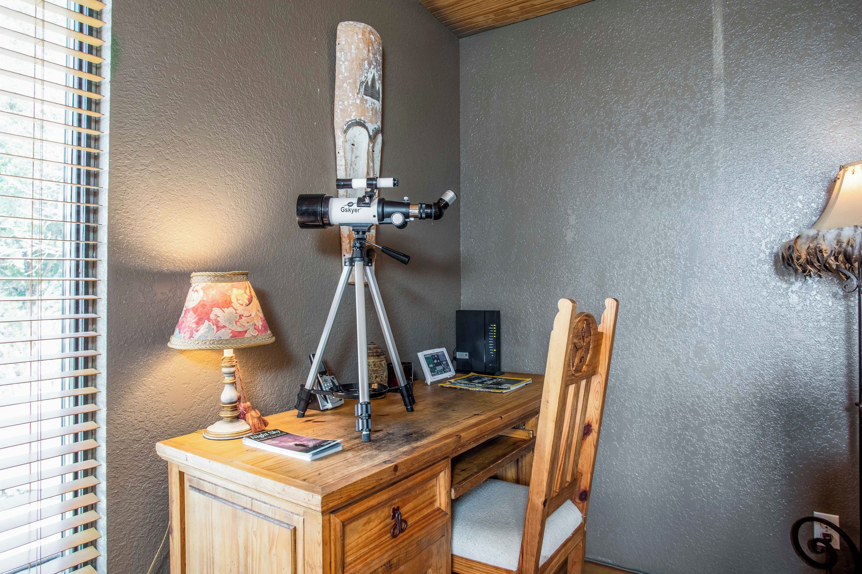 Un escritorio de madera con un telescopio, una lámpara y una silla.