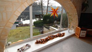 Une pièce dotée d’une fenêtre en arc de pierre donnant sur un lac, d’un banc en bois et d’un ornement décoratif en forme d’étoile.
