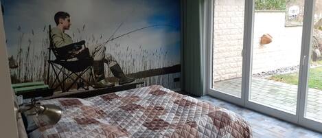 Une chambre avec un grand lit, une fresque représentant un homme qui pêche et une porte-fenêtre coulissante donnant sur un espace extérieur.
