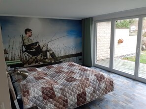 A bedroom with a large bed, a mural of a man fishing, and a sliding glass door leading to an outdoor area.