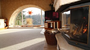 Un salon chaleureux avec une cheminée en pierre, une grande fenêtre décorée d’une étoile et une arche en pierre.