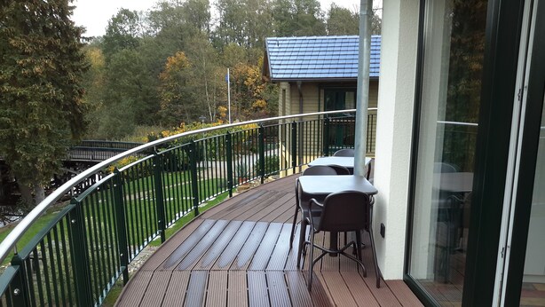 Een houten terras met een metalen hekwerk, een tafel en stoelen.