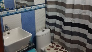 A bathroom with a white sink, a toilet with decorative stones, a striped shower curtain, and a mirror above the sink. - Daily Apartment in Iquique in my house. (Iquique)