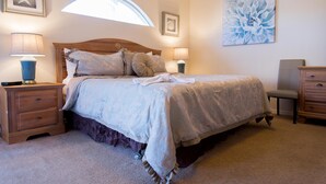 Een slaapkamer met een groot bed, twee nachtkastjes, een stoel en een wandlamp.