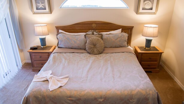 Een net opgemaakt bed met een bloemenprintdeken, twee bedlampen en een foto van een zeester aan de muur.