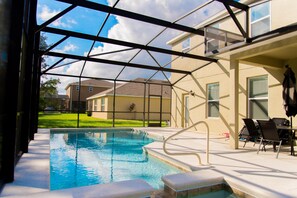 An indoor swimming pool with clear glass walls, a patio area with chairs, and a view of neighboring houses. - Trafalgar Retreat by Orlando Short Term (Kissimmee)