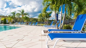 A poolside area with blue lounge chairs, a tiled walkway, and palm trees. - Trafalgar Retreat by Orlando Short Term (Kissimmee)