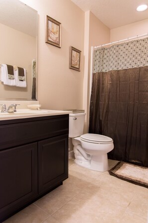 A bathroom with a dark wooden vanity, a white toilet, and a shower curtain. - Trafalgar Retreat by Orlando Short Term (Kissimmee)