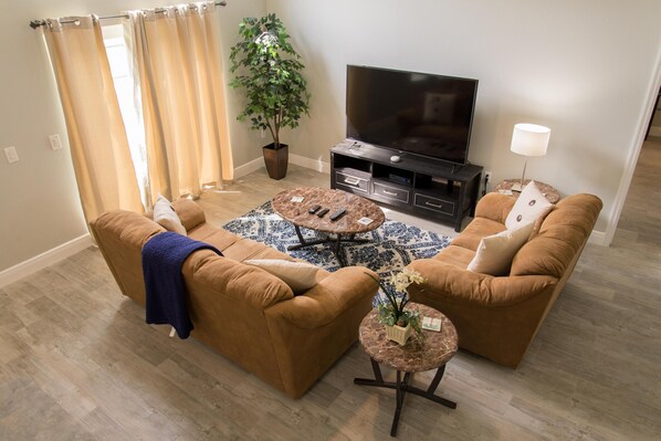 A living room with two brown sofas, a coffee table, a TV, a potted plant, and a lamp.