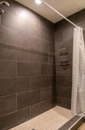A shower area with dark tiles, a showerhead, a towel rack, and a polka-dotted shower curtain. - Palm Studio by Orlando Short Term (Kissimmee)