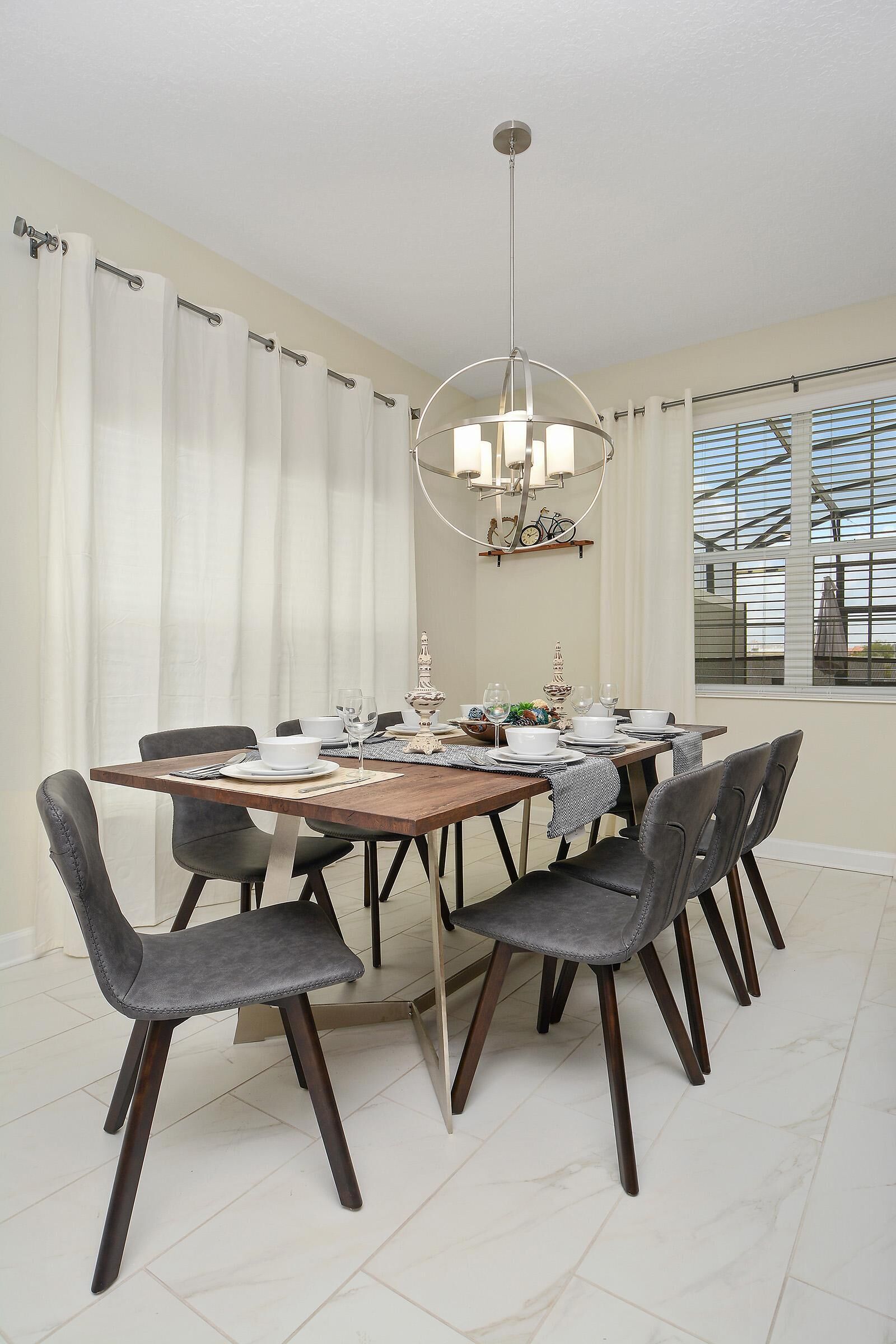 Un coin repas avec une table en bois, des chaises à revêtement gris, de la vaisselle blanche et un lustre.