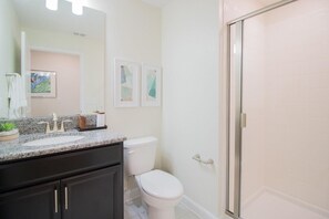 Ein Badezimmer mit Marmorwaschtisch, Toilette, Duschkabine mit Glastür und gerahmten Bildern an der Wand.