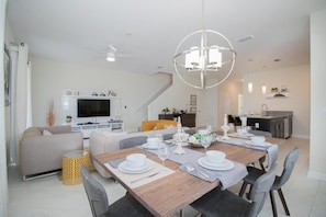 Una sala de estar moderna con comedor, televisor y una escalera que sube a otro nivel.