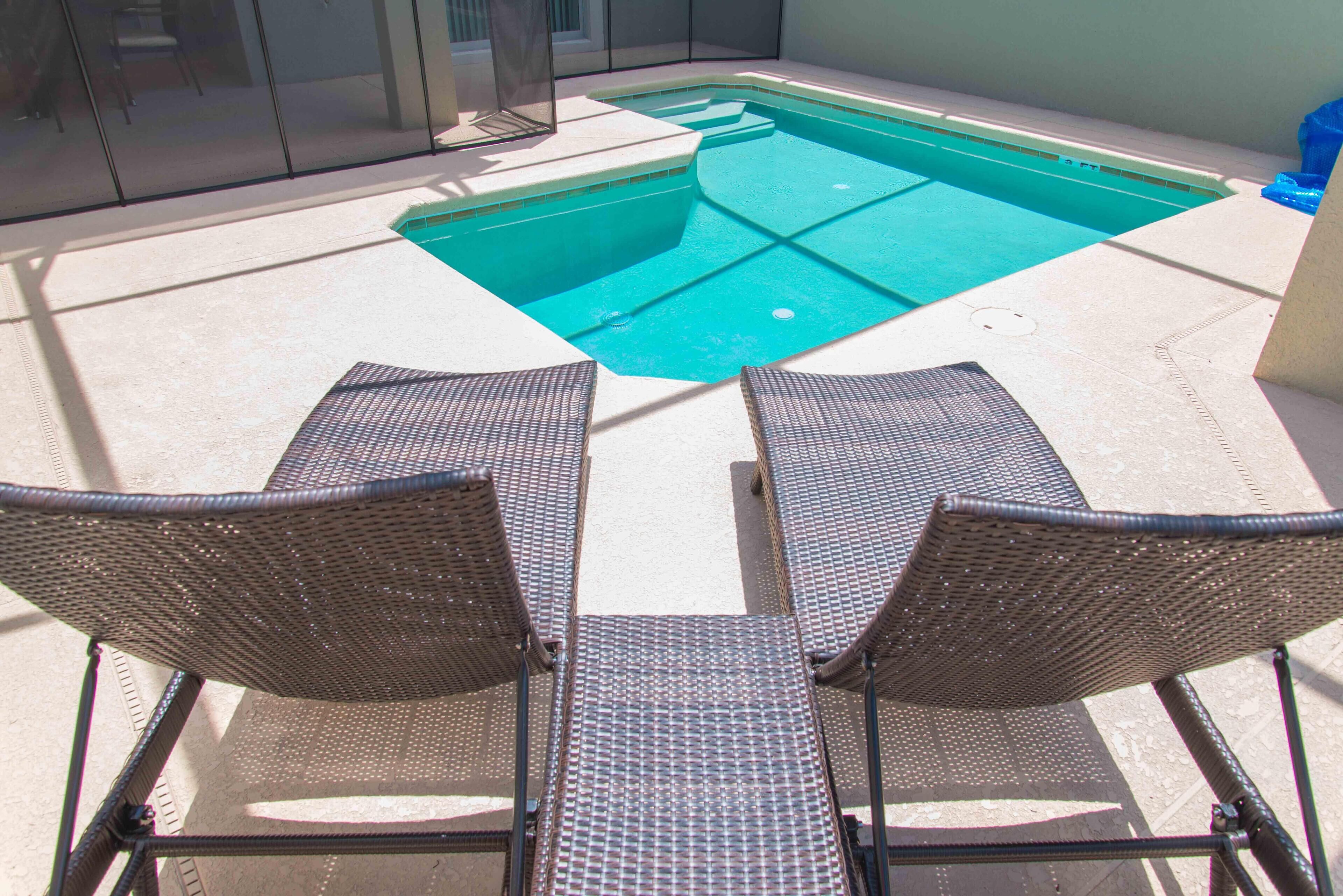 Una piscina con dos sillones de mimbre frente a ella.