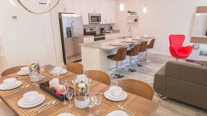 A modern kitchen with stainless steel appliances, a dining area with a buffet setup, and a bright red chair. - Gatsby Storey by Orlando Short Term (Kissimmee)