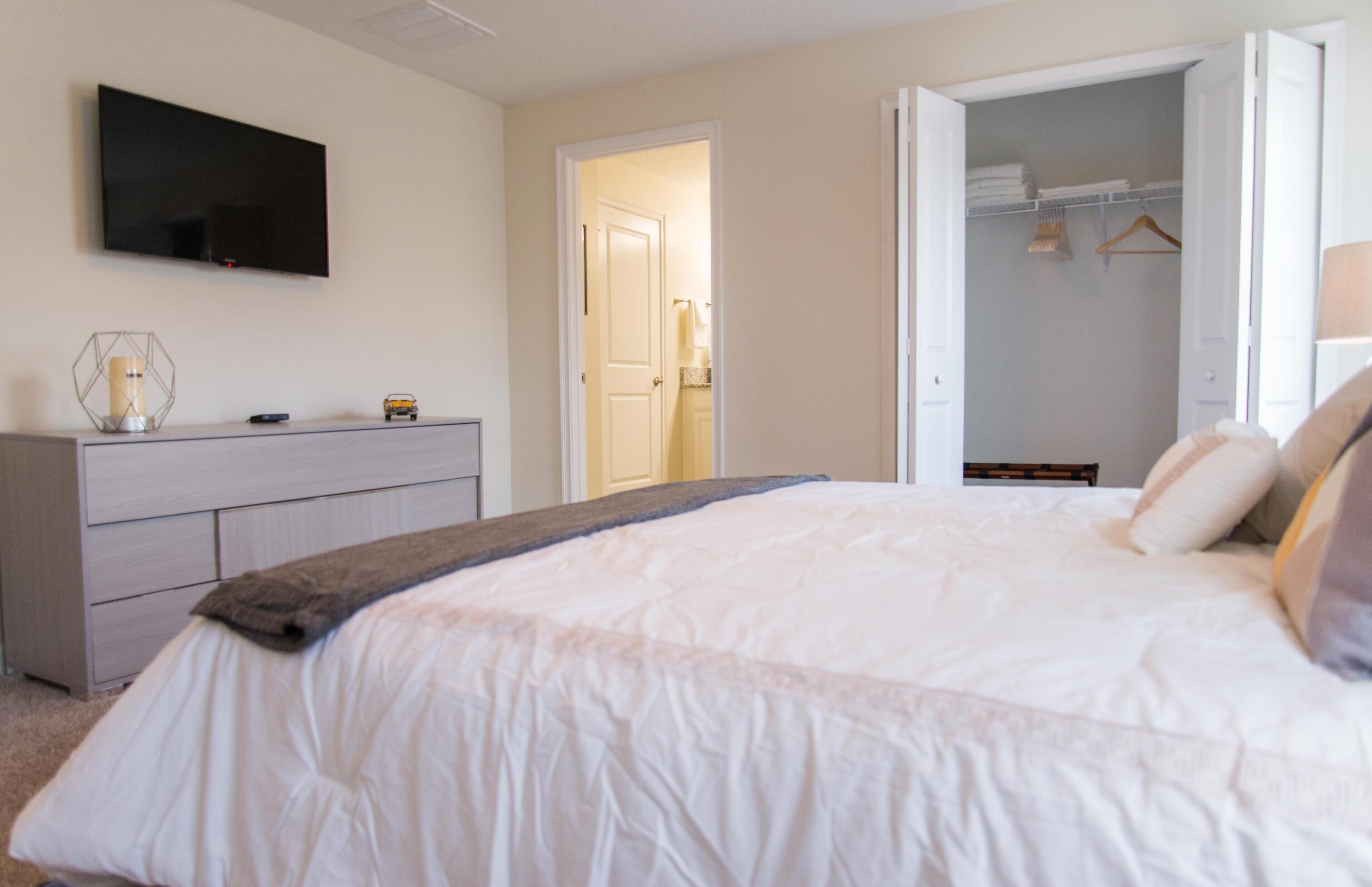 Een slaapkamer met een bed, een dressoir, een televisie en een open kast.