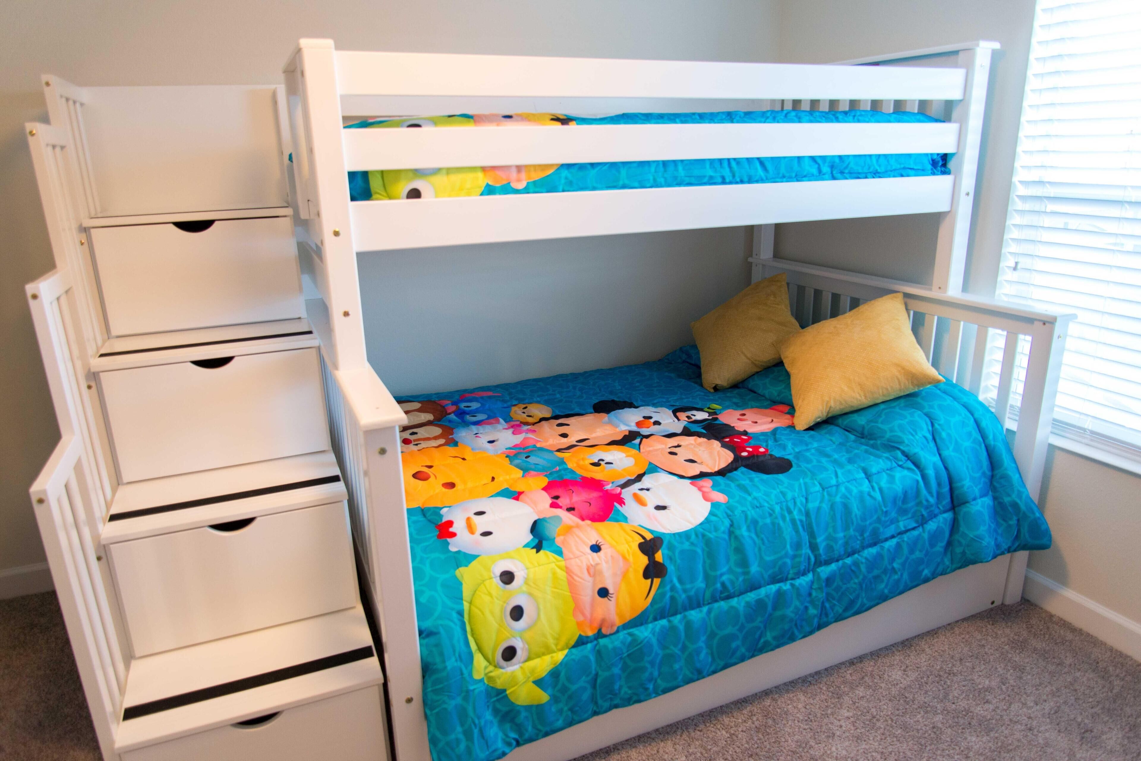 Una cama litera con un edredón colorido, cajones blancos para guardar cosas y dos almohadas.