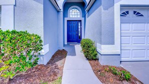 A house with a blue door, white garage door, and a pathway leading to the entrance. - Paradise Island by Orlando Short Term (Kissimmee)