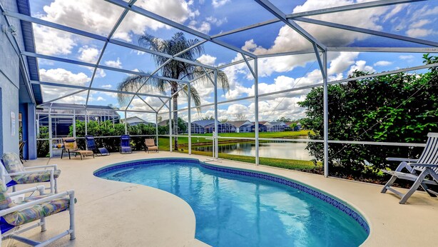 A covered swimming pool with lounge chairs, a palm tree, and a view of a golf course. - Paradise Island by Orlando Short Term (Kissimmee)