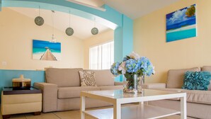A living room with a beige sofa, a white coffee table, and a painting of a beach scene. - Paradise Island by Orlando Short Term (Kissimmee)
