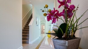 Um corredor com piso de mármore, um vaso com flores cor-de-rosa e uma escadaria ao fundo.