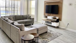 Uma sala de estar moderna com sofá seccional, televisão na parede e uma pequena mesa de centro.