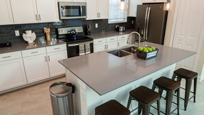 Cozinha moderna com armários brancos, geladeira de aço inoxidável, micro-ondas e uma ilha grande com banquetas.