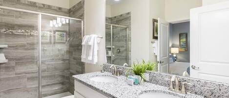 Un baño moderno con dos lavamanos, cabina de ducha de vidrio y un espejo grande.