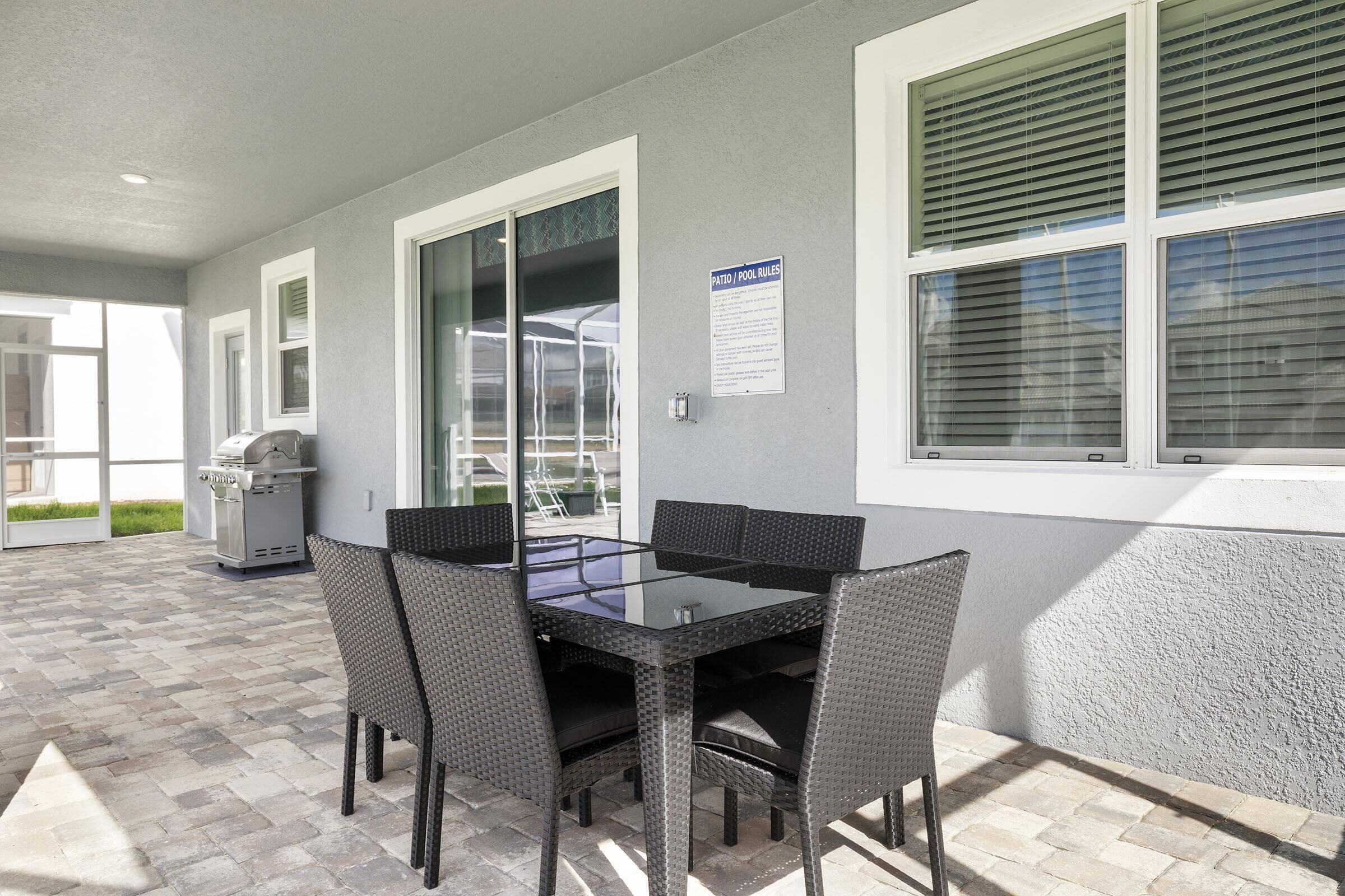 An outdoor patio area with a glass-top table and wicker chairs, a grill, and a sign indicating patio pool rules.