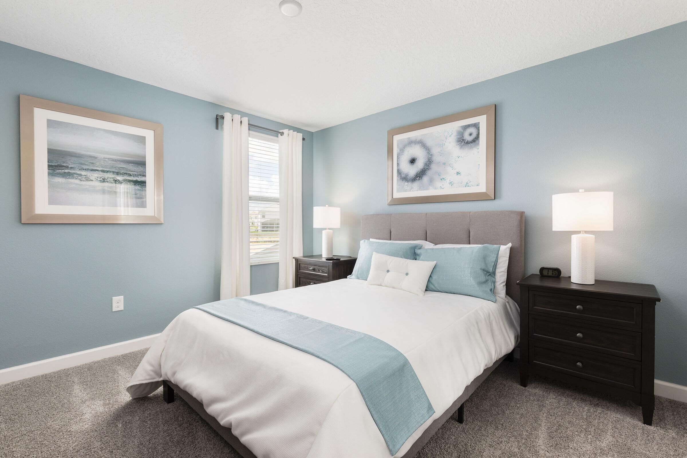 A bedroom with a bed, two nightstands, a window with curtains, and two framed pictures on the wall.