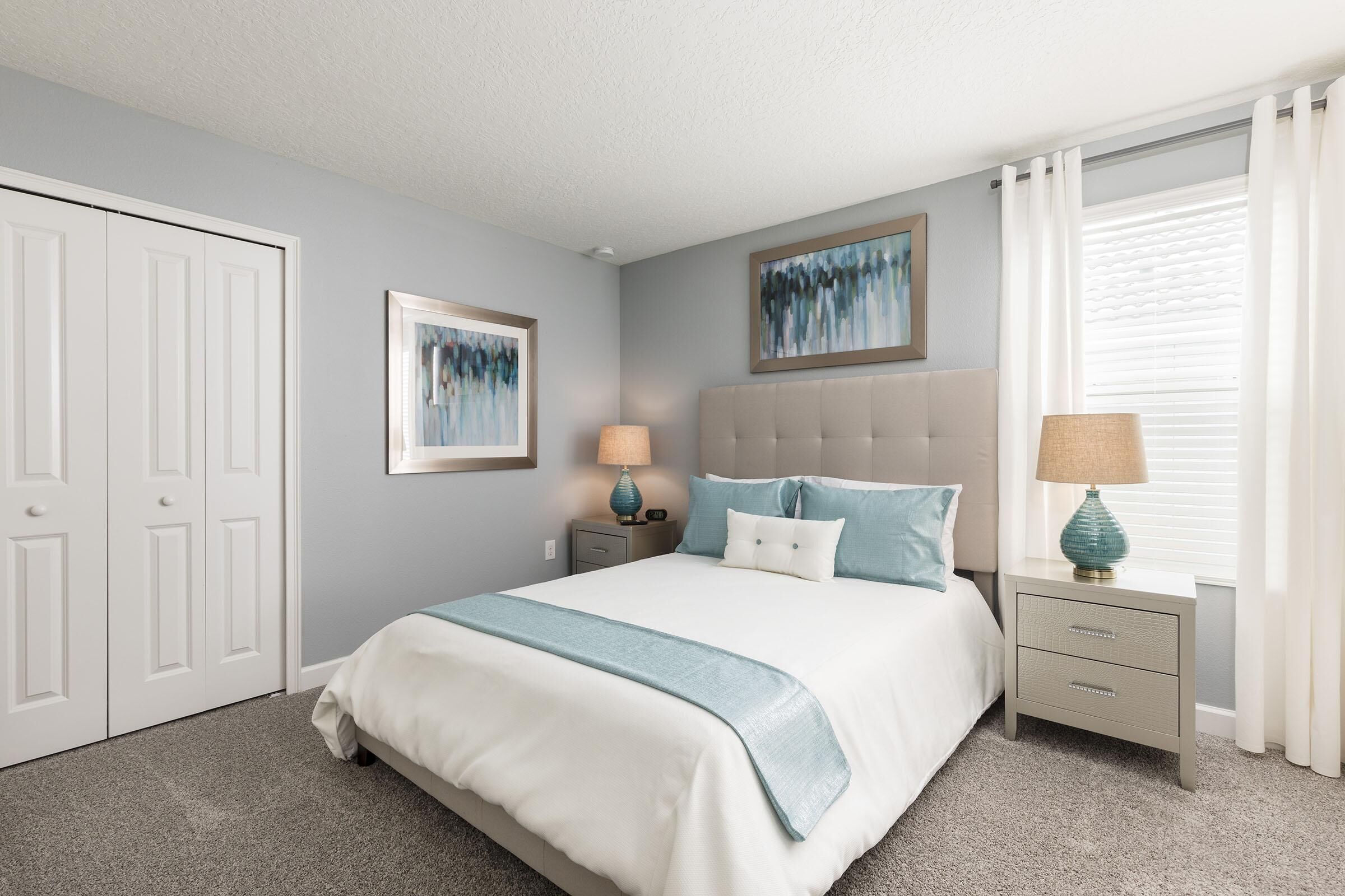 A bedroom with a bed, nightstands, a lamp, a framed picture, and a window with curtains.