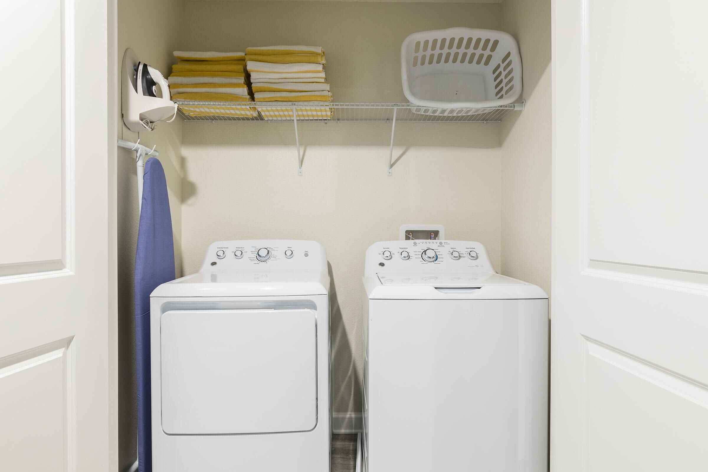 A laundry room with two white front-loading washing machines, a drying rack, and a basket.