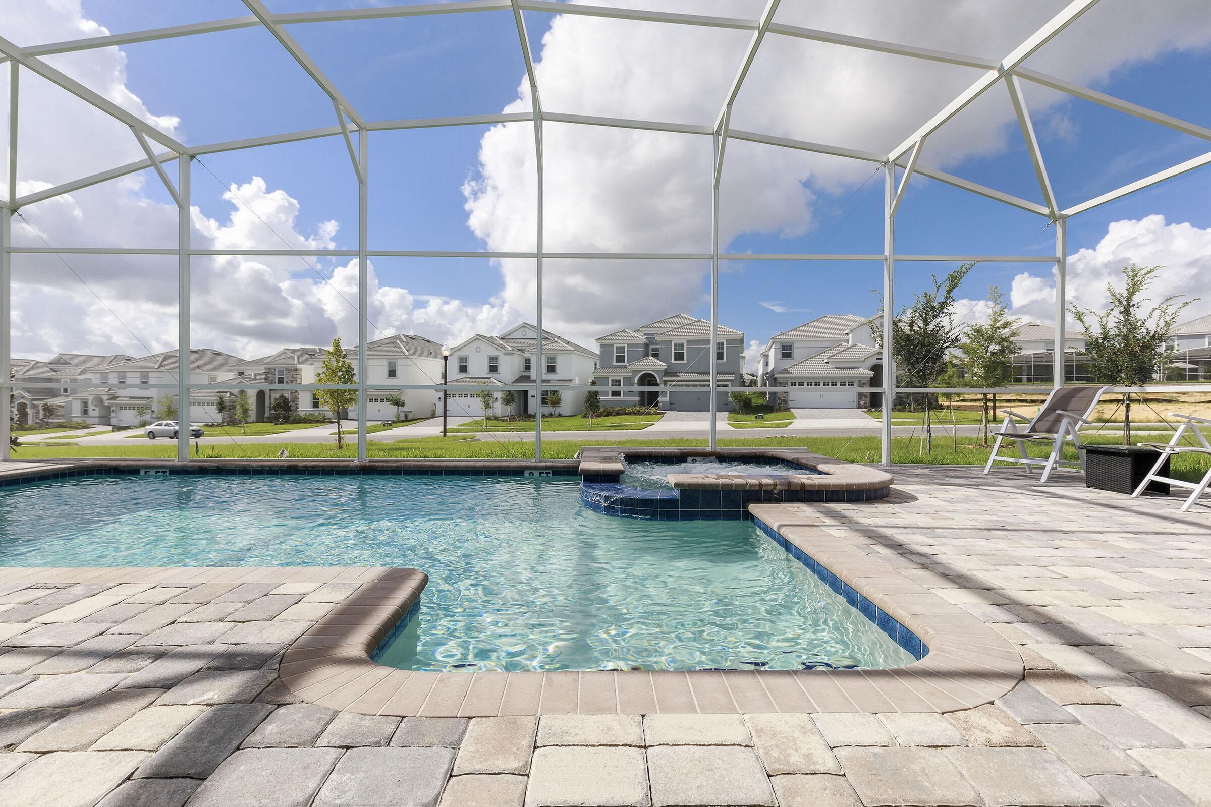 A swimming pool with a covered area, stone tiles, and a view of houses in the background.