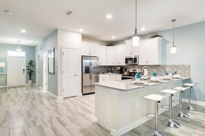 Una cocina moderna con armarios blancos, electrodomésticos de acero inoxidable y una isla central con taburetes de bar.
