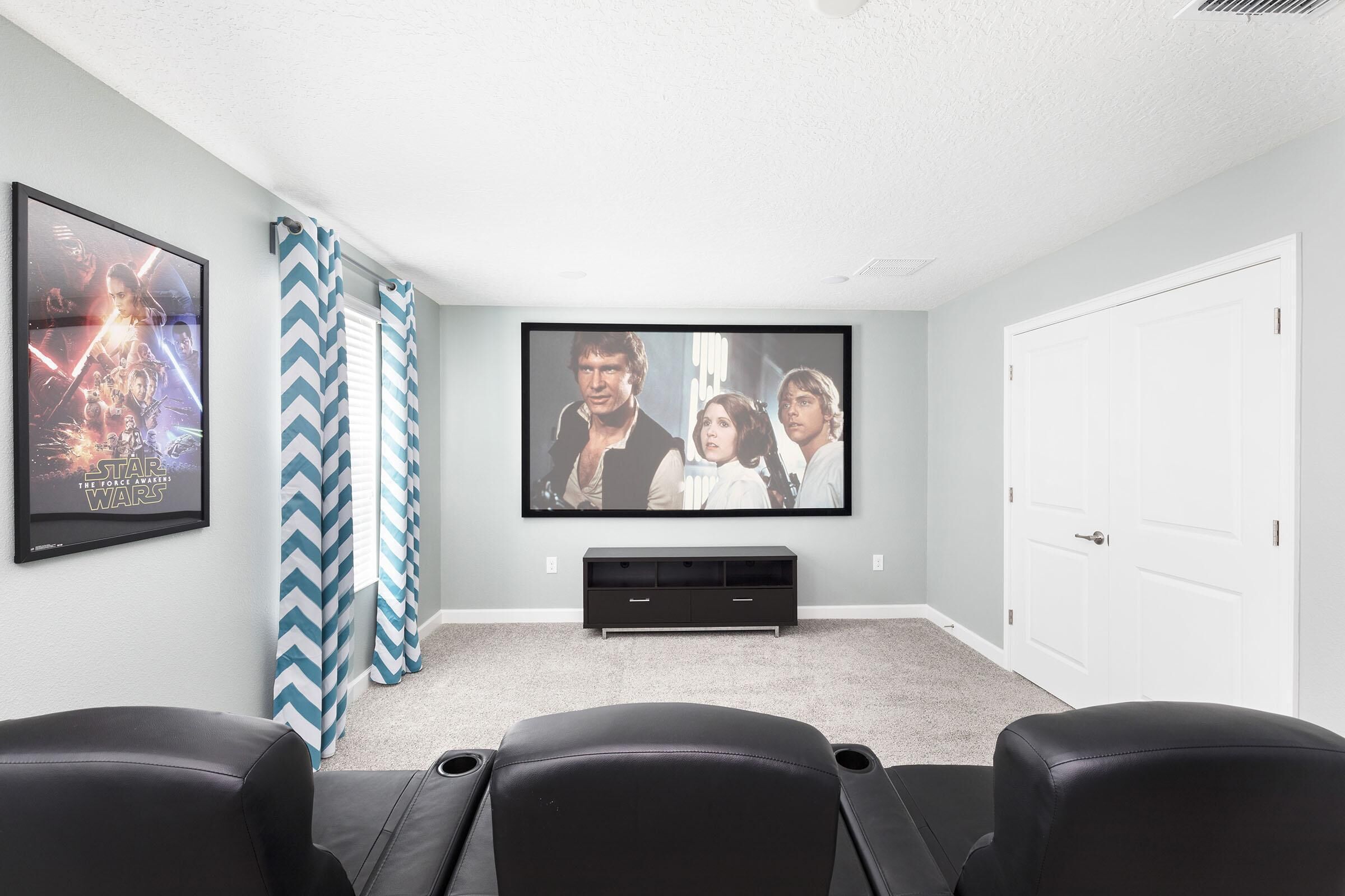 A home theater room with a large flat-screen TV, a black entertainment unit, and three black leather recliner chairs.