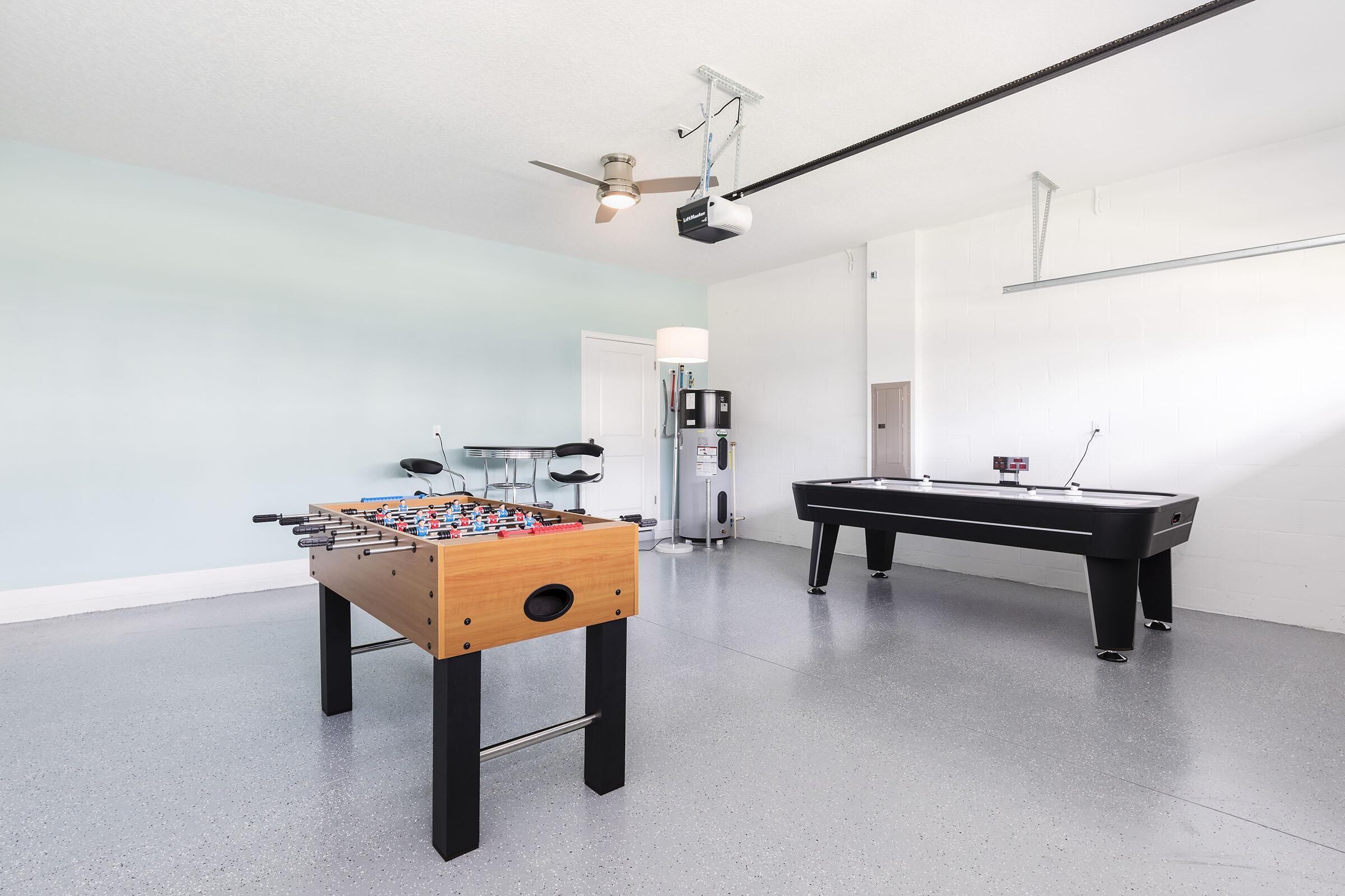 A room with a foosball table, a pool table, and a ceiling fan.