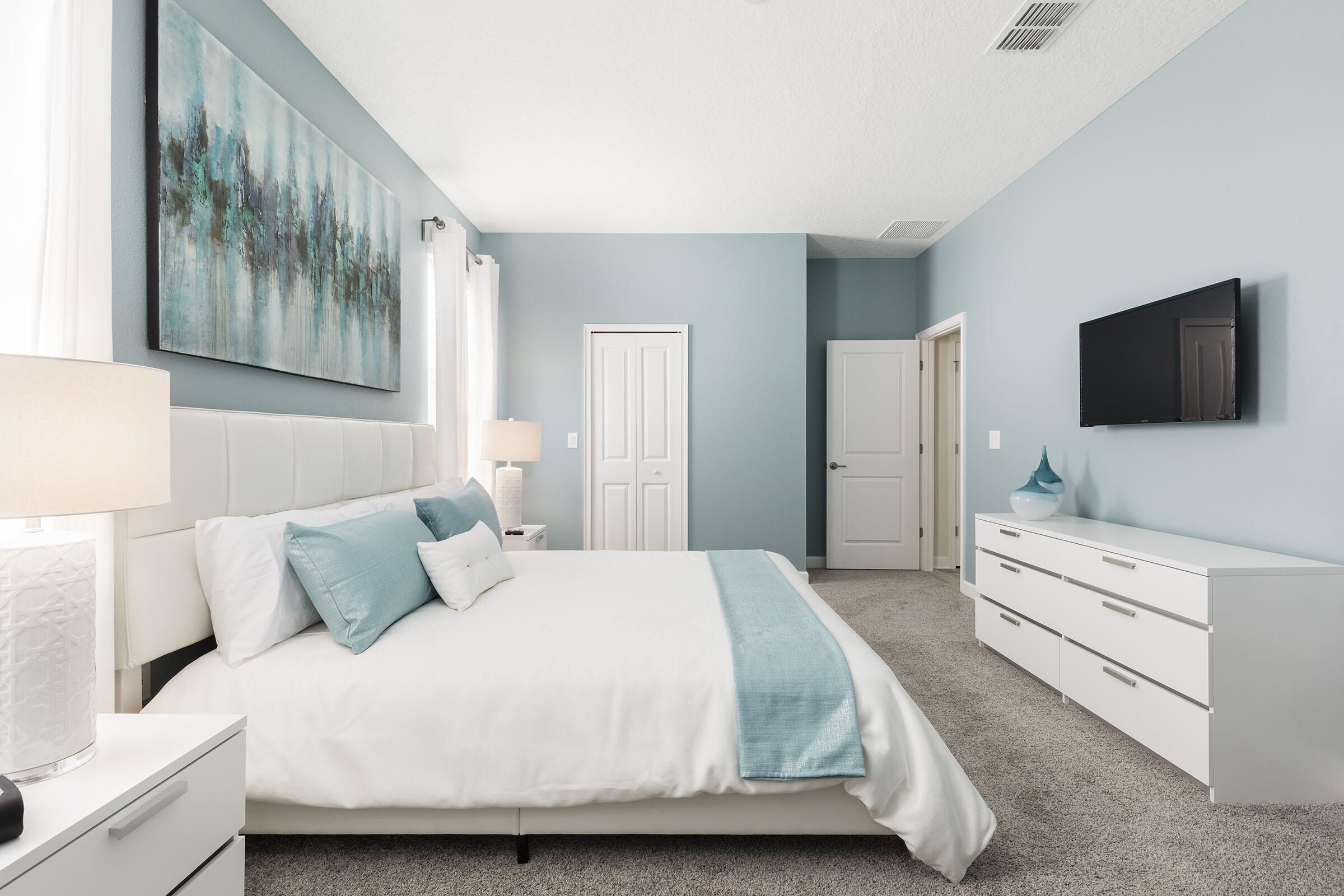 Une chambre à coucher avec un lit, des tables de chevet, une commode, un téléviseur et une porte.