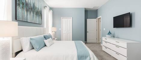 A bedroom with a bed, bedside tables, a dresser, a TV, and a door.